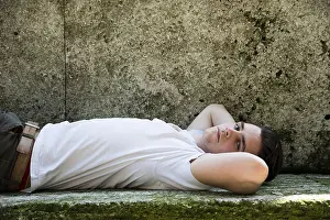 Young Man Looking At Camera Drucke: Handsome young man lying down on stone blocks