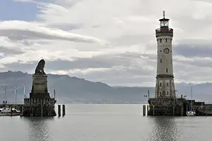 Lion Statue Germany Drucke: A harbor with a lighthouse and a lion statue under a dramatic sky