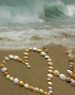 Muschel Drucke: Zwei Herzen aus Muscheln auf einer Strand mit schweren Wellen im Hintergrund.