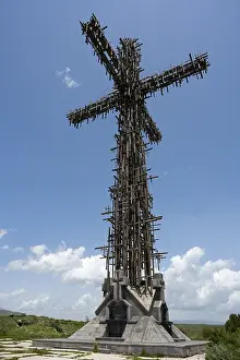 Deserted Memorial Site Drucke: High metal cross with complex structure under a blue sky with clouds