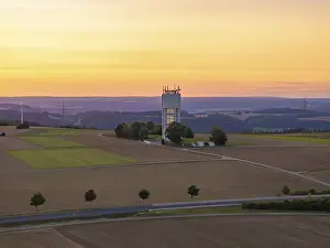 Deserted Farmland At Sunset Drucke: Hilly landscape with fields and a tower in the sunset light