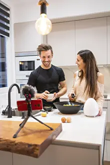 Happy Couple In The Kitchen Drucke: Horizontal photo with copy space of a couple cooking and using mobile phone for streaming tutorial