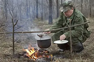 Outdoor Food Photography Drucke: The hunter makes a dinner on a bonfire