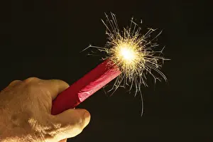Ein entzündeter Feuerwerkskörper wird mit einer Hand gehalten.