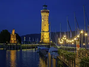 Drucke von Ein beleuchteter Leuchtturm in der Nacht, umgeben von Booten und Lichtern im Hafen, Meersburg, Bodensee, Deutschland Bodensee Drucke: Ein beleuchteter Leuchtturm in der Nacht.