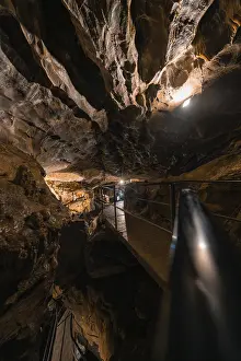 Cave Landscape Photography Drucke: Illuminated path in a cave, surrounded by rocks and darkness