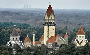 Saxony Church Building Drucke: Impressive building with towers and red roofs surrounded by forests and a diffuse sky in the background