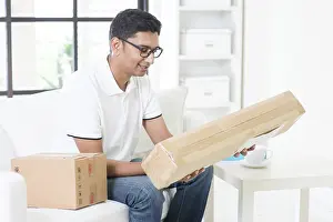 Handsome Indian Guy Looking At Camera Drucke: Indian guy received an express parcel and checking the box at home