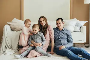 Family Bonding Moments Drucke: Junge gluckliche Eltern, die mit kleinen Kindern auf dem Boden sitzen und in die Kamera schauen Junge gl