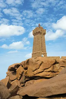 Blue Sky Lighthouse View Drucke: A lighthouse perched on massive rocks under a blue sky