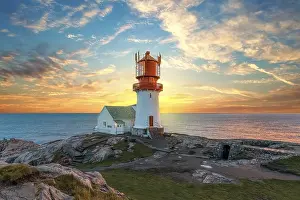 Lighthouse At Sunset Drucke: Lighthouse surrounded by rocks at sunset