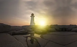 Lighthouse At Sunset Drucke: Lighthouse surrounded by rocks at sunset