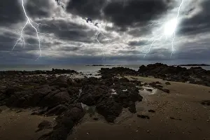 Thunderstorm Atmosphere Drucke: Lightning over the sea with rocks in the foreground