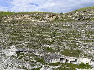 Drucke von Kalksteinfelsen mit sichtbaren Höhlenstrukturen, grüne Landschaft unter blauen Wolken, Luftaufnahme, Höhlenwohnhäuser, Alt-Orhei, Orheiul Vechi, archäologischer Fundort Moldawien Drucke: Kalksteinfelsen mit sichtbaren Höhlenstrukturen.