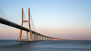 Portugal Tourist Attraction Drucke: A long cable-stayed bridge spans over water under a gradient sunset sky