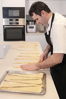 Caucasian Man In Kitchen Drucke: A man baking croissants picking up the triangular cuts from the puff pastry
