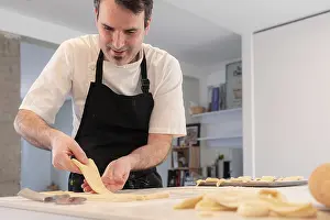 Male Baker At Home Drucke: A man baking croissants picking up the triangular cuts from the puff pastry