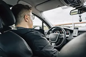 Urban Road Safety Drucke: A man drives a car using a navigation application installed on a smartphone