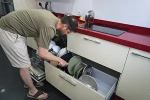 Contemporary Kitchen Design Drucke: A man efficiently organizing kitchen cookware in a modern kitchen
