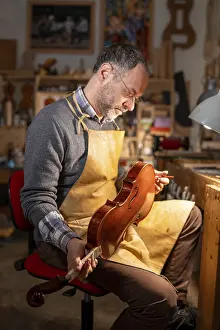 Bilder Datiert 3. Dezember 2024: Ein Mann untersucht ein Violin in einem Werkstattsetting mit einer konzentrierten Miene unter warmem Licht