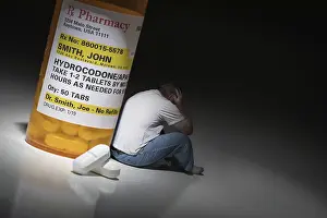 Addictive Drug Abuse Drucke: Man holding head sitting next to hydrocodeon pills and bottle
