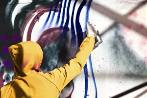 Straßenkünstler Drucke: Ein Mann in einem Schal malt Graffiti an einer Wand.