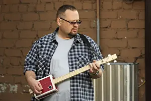 Vintage Guitar Player Drucke: Man playing his three string cigar box guitar