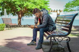 Man Checking Phone Drucke: Man sitting on a bench checking his phone