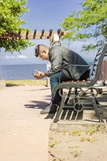 Man Checking Phone Drucke: Man sitting on a bench checking his phone