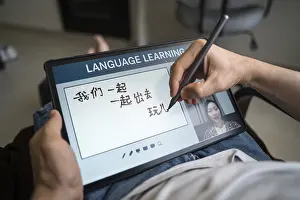 Language Training At Home Drucke: A man studies Mandarin at home using a tablet for online language learning