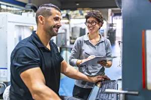 Business Teamwork Drucke: Manager and worker talking while working using computer in a cnc metal factory