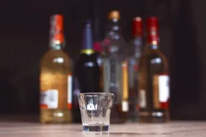 Drucke von Mannheim, Deutschland, Juni 2019: Leeres kleines Schnapsglas vor mehreren verschwommenen verschiedenen starken Spirituosen-Alkoholflaschen im dunklen Hintergrund Mannheim Drucke: Mannheim, Deutschland