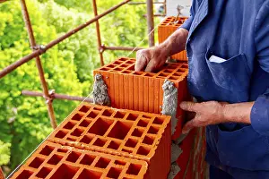 Construction Site Worker Drucke: Mason, bricklayer worker is using red blocks to mount a wall next the string line to be straight