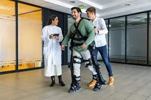 Young Adults With Disability Drucke: Mechanical exoskeleton, female doctor with device walking with disabled person with robotic skeleton in rehabilitation