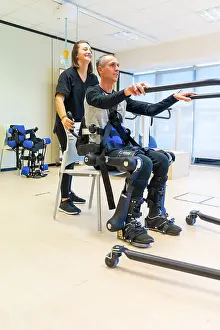 Mechanical Exoskeleton Drucke: Mechanical exoskeleton. Female physiotherapy doctor assistant lifting disabled person with robotic skeleton to get up