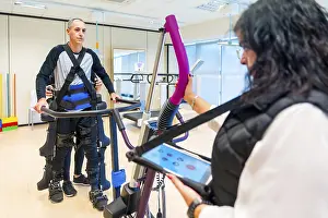 Mechanical Exoskeleton Drucke: Mechanical exoskeleton. Female physiotherapy medical assistant with disabled person lifted with robotic skeleton