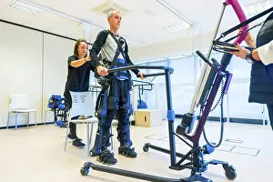 Mechanical Exoskeleton Drucke: Mechanical exoskeleton. Female physiotherapy medical assistant lifting disabled person with robotic skeleton