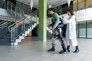 Mechanical Exoskeleton Drucke: Mechanical exoskeleton, female doctor physiotherapist walking with disabled person helped by robotic skeleton