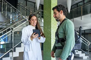 Mechanical Exoskeleton Drucke: Mechanical exoskeleton, female physiotherapist doctor talking with tablet with disabled person with robotic skeleton