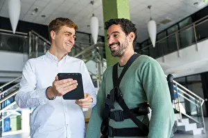 Physical Therapy Treatment Drucke: Mechanical exoskeleton, physiotherapist looking at consultation with tablet with disabled person with robotic skeleton