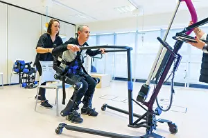 Physiotherapy Equipment Drucke: Mechanical exoskeleton. Female physiotherapy medical assistant lifting disabled person with robotic skeleton
