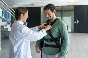 Mechanical Exoskeleton Drucke: Mechanical exoskeleton, female physiotherapist doctor putting tapes on disabled person with robotic skeleton