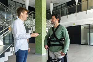 Mechanical Exoskeleton Drucke: Mechanical exoskeleton, physiotherapist looking at consultation with tablet with disabled person with robotic skeleton