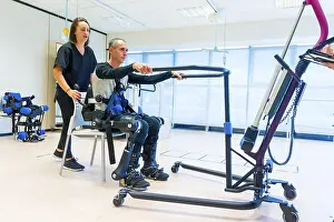 Mechanical Exoskeleton Drucke: Mechanical exoskeleton. Female physiotherapy doctor assistant lifting disabled person with robotic skeleton to get up