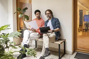 Teamwork And Collaboration Drucke: Two men discuss documents and digital content in a bright