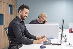 Businessman On Phone Drucke: Men using computer and talking to the mobile in a coworking