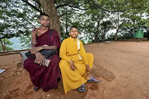 Southeast Asian Nature Photography Drucke: A monk and a boy sit relaxing on a sandy surface under a tree in the forest