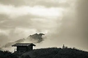 Female Hiker Drucke: Mountain hut with bench and climber and dramatic clouds in the background