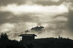 Female Hiker Drucke: Mountain hut with bench and climber and dramatic clouds in the background