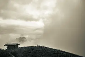 Dramatic Clouds Drucke: Mountain hut with bench and climber and dramatic clouds in the background